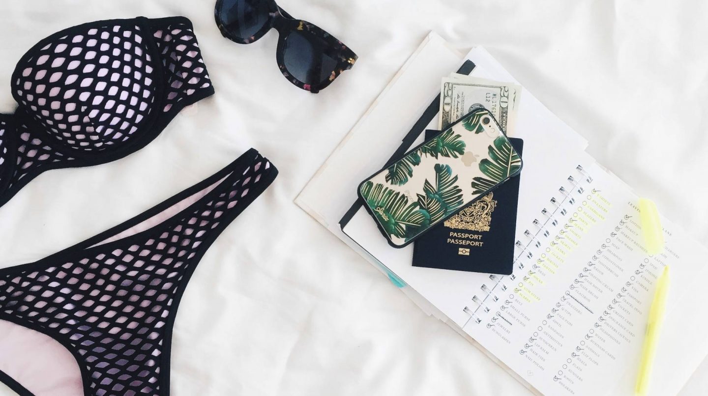 swimwear on a bed with diary, passport, sunglasses and iPhone