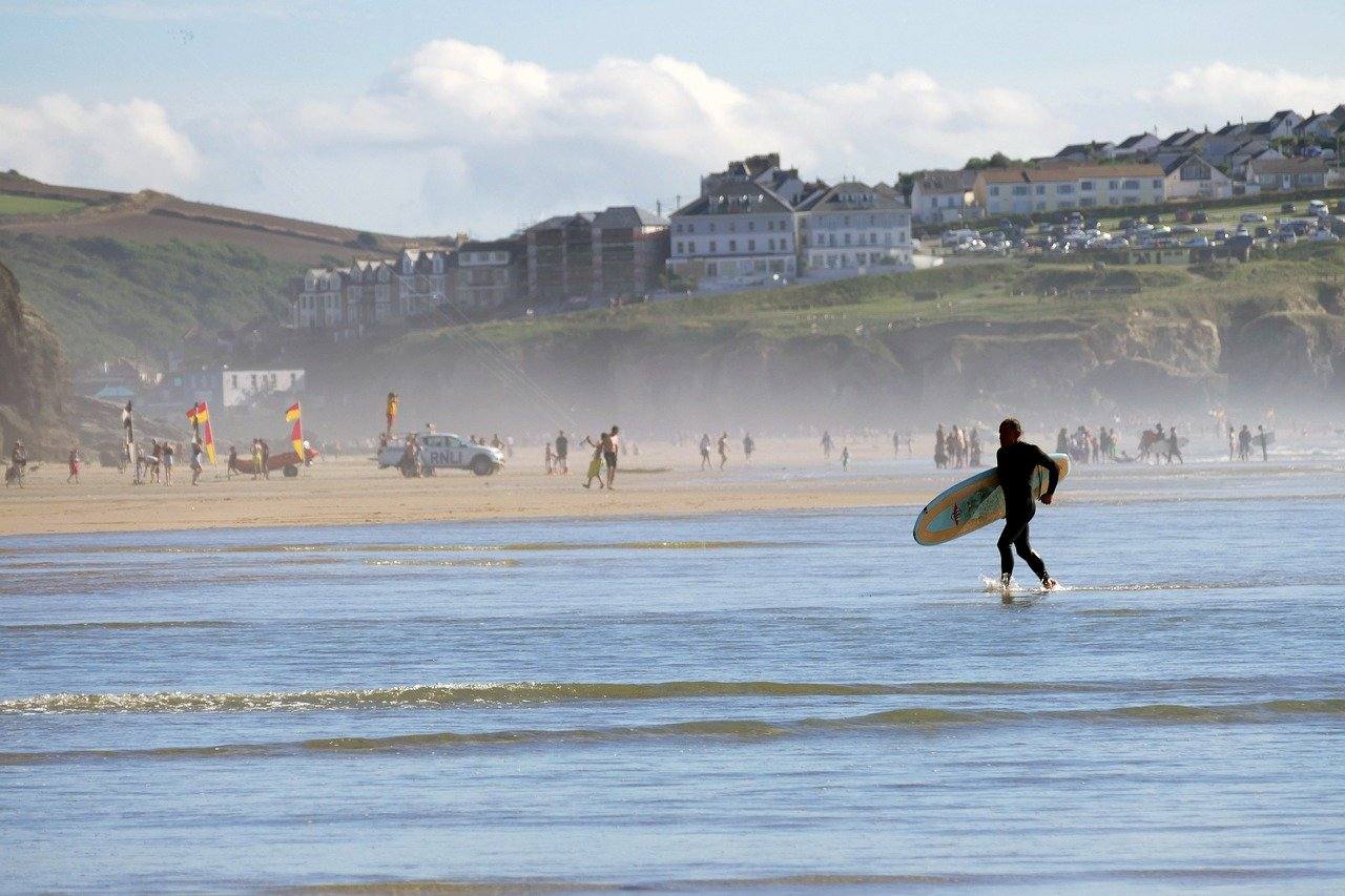 Man carrying a surfboard into the water on a beach