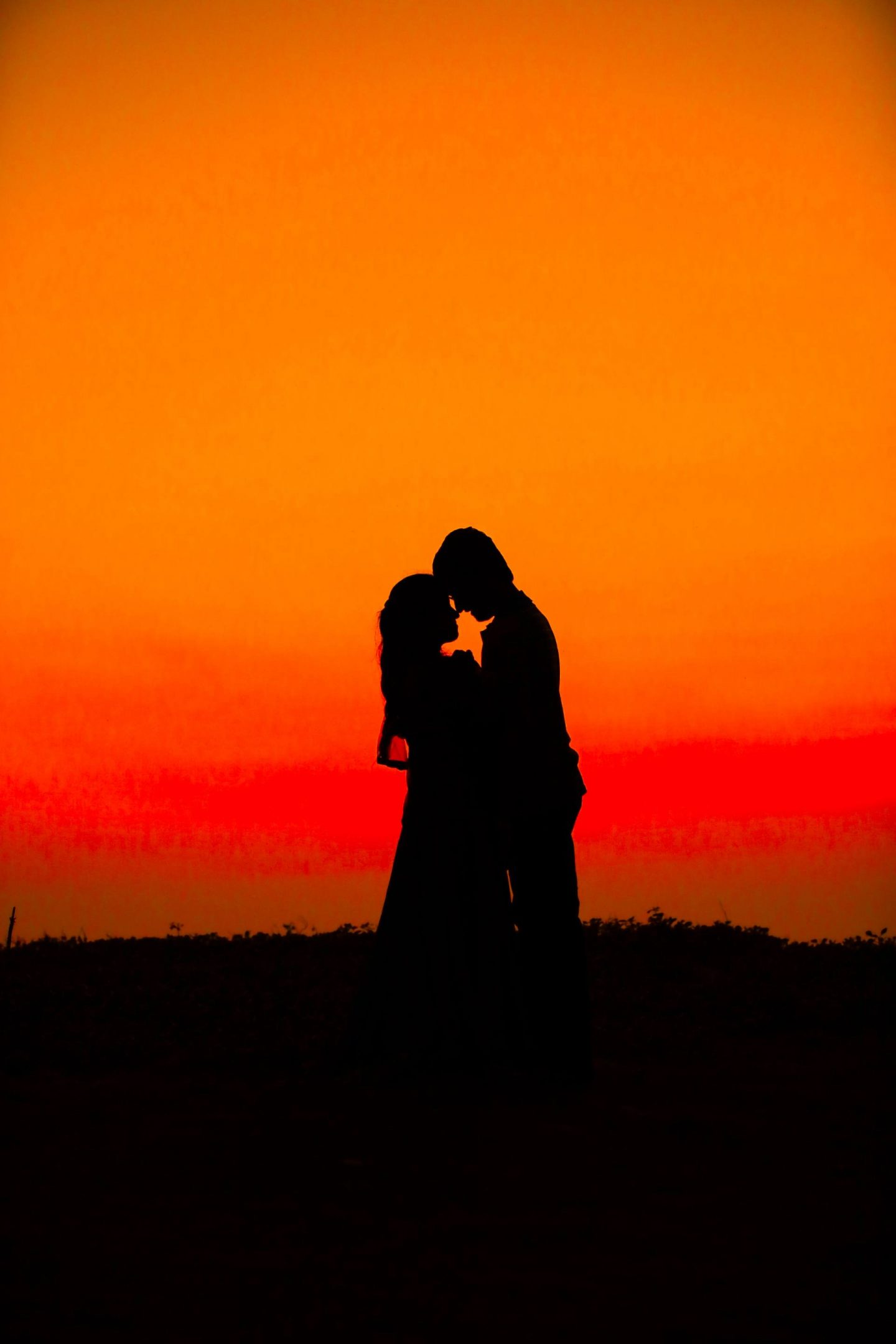 The silhouette of a couple standing in each other's embrace, forehead-to-forehead.